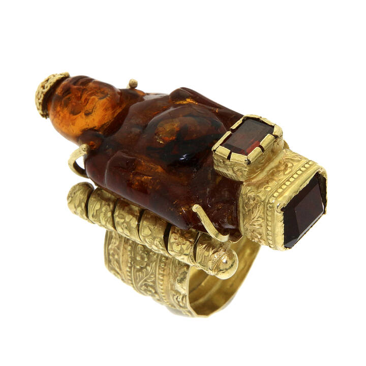 ANELLO - Anello in oro giallo, sommità con ambra lavorata a forma di budda; due granati taglio rettangolare a decoro
