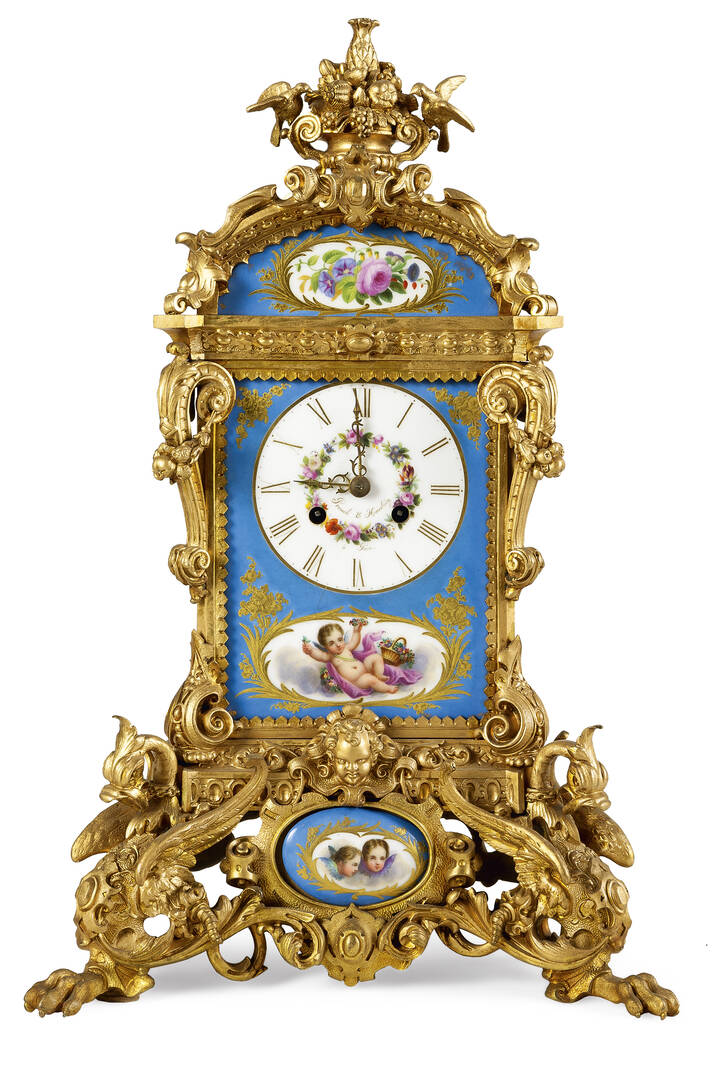 OROLOGIO DA TAVOLO - Orologio da tavolo in bronzo dorato e porcellana di Sevres, fine XIX secolo. Porcellana a fondo azzurro con dipinti fiori e putti, decori in oro zecchino<br>Quadrante firmato 'Promoli e Hausbeirg'<br>Ridorato