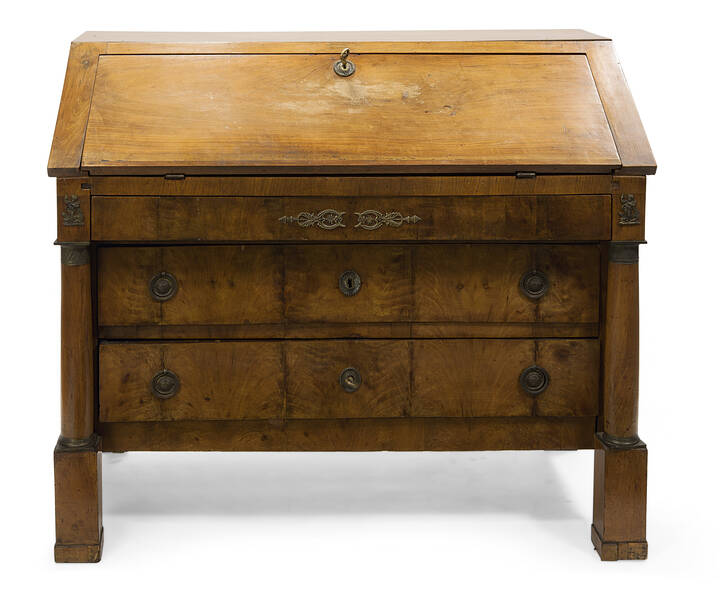 RIBALTA - Cassettone a ribalta in noce, epoca Impero, inizi XIX sec. fronte lastronato in piuma di noce e quattro tiretti, ai lati colonne guarnite da bronzi. Piedi rettangolari. All'interno della calatoia quattro tirettini e due colonnine. Difetti alla calatoia.<br>